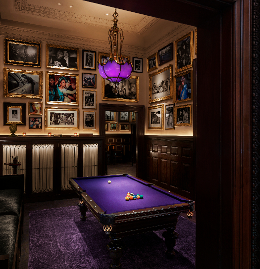 Elegant billiards room with purple felt table, ornate chandelier, and gallery wall of framed artwork