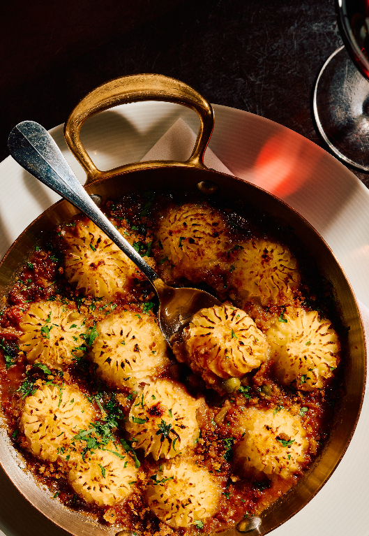 Shepherd’s Pie in a copper pan with dark golden crust, garnished with herbs in a rich sauce, with serving spoon