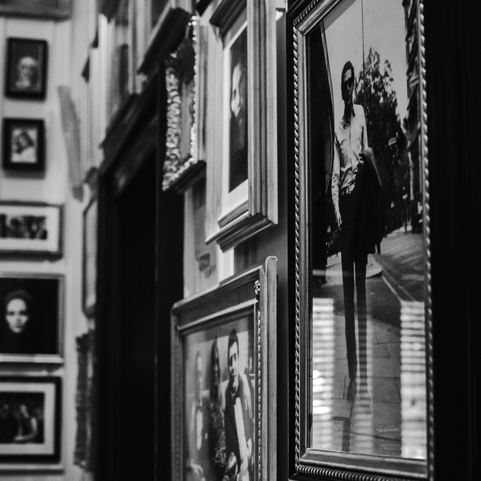Black-and-white wall display of framed photographs, including a prominent image of a person in a reflective mirror.
