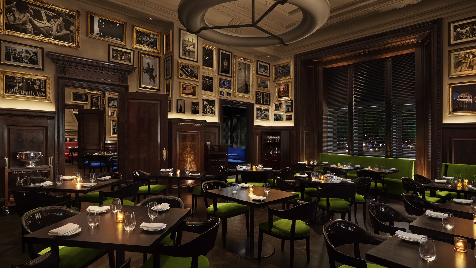 Elegant restaurant with wooden tables, green chairs, wall artwork, and ambient lighting.